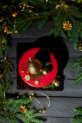 A vibrant red cake sits elegantly on a dark surface, decorated with golden orbs and festive greenery, creating a joyful atmosphere with twinkling holiday lights.
