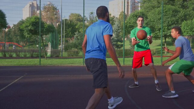 Motivated sporty fit black male basketball player receiving pass from teammate, making field goal attempt to score two points while multiracial athletes playing streetball game outdoors.