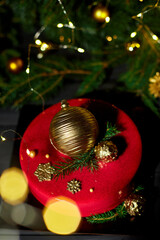 A vibrant red cake sits elegantly on a dark surface, decorated with golden orbs and festive greenery, creating a joyful atmosphere with twinkling holiday lights.