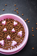 Dog food in pink bowl with heart shapes, top view on dark surface.