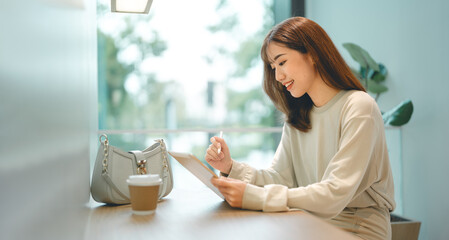 Adult asian business woman using digital tablet working and relax at cafe sitting near window