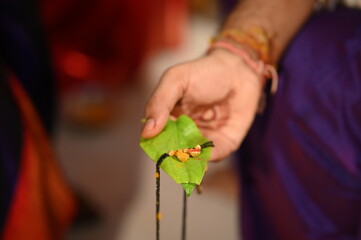 hand of Groom holding golden mangalsutra on leaf. Wedding indian jewelery. Bride and groom hands in mangalsutra ceremony. Henna hands. Indian wedding rituals. Maharashtra wedding	