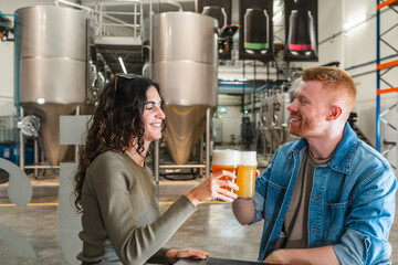Happy couple toasting beer glasses while visiting a modern craft brewery, exploring the brewing...