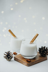 Two glasses of creamy winter drink with cinnamon sticks, pine cones, and star anise