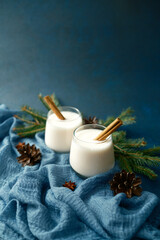 Creamy winter drinks with cinnamon sticks and pine cones on blue fabric