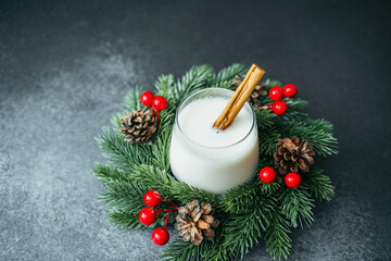 Creamy winter drink with cinnamon stick nestled in festive fir garland with pinecones © reddish