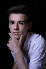 Close-up portrait of a young man in a white shirt with hand on chin looking seriously at the camera