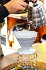 A barista prepares coffee using the pour-over method by pouring water into a funnel with a filter...
