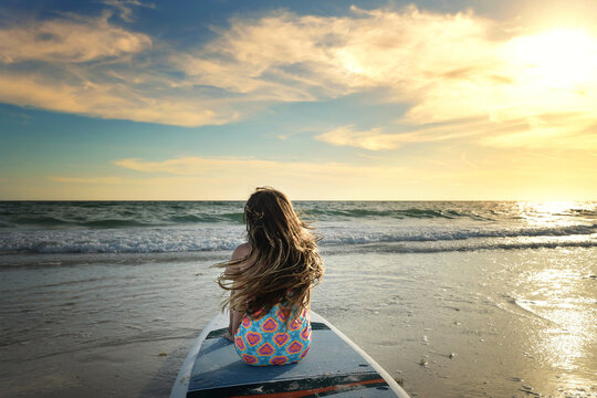 Side view young girl sitting on paddle board hair blowing sunset