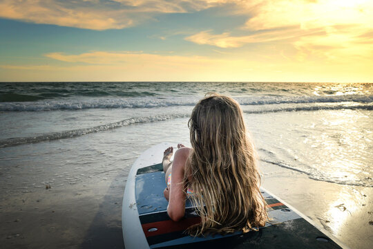 Behind young girl sitting on paddle board at sunset Gulf of Mexi