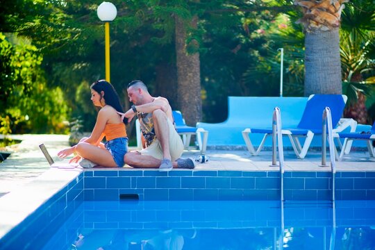 supportive man scratching back of woman working on laptop next to pool