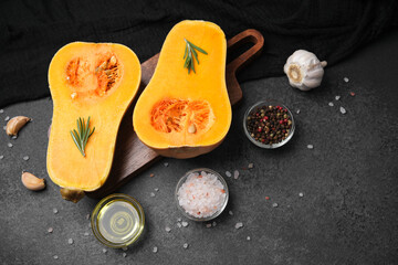 Butternut squash cut in half with rosemary, garlic, peppercorns and salt on dark surface