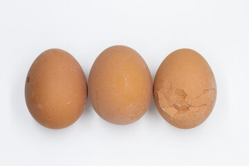 two whole eggs and one broken egg are lying in a row on a white background