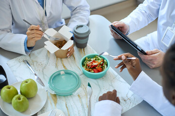 Cropped shot of hands of unrecognizable healthcare professionals having a meal around table and...