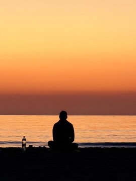 Person meditating on beach at sunset in peaceful solitude by the sea horizon. 