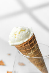 Closeup of waffle cone with creamy vanilla ice cream resting in clear glass on bright background with crumbs