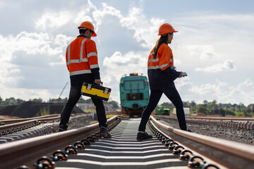 Two rail engineers in orange safety jackets and helmets walk across a newly built railway track...