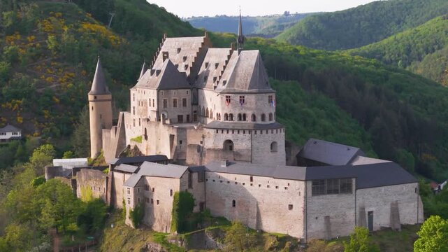 approaching vianden castle chateau de round arches old historical site green yellow trees surrounding hills flags walls complete reveals forward drone shot view luxembourg 