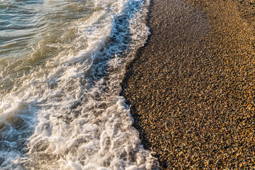 Sparkling waves of the sea roll over the sea pebbles of the beach. Beautiful seascape. A copy of the space. Atmospheric realistic photo.
