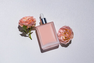 Blank mockup of rectangular cosmetic bottle with pipette on white background with delicate rose blossoms. top view. layout to advertise your product.
