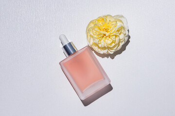 Matte rectangular bottle with pipette with serum, cosmetic product on a light background with a yellow rose head. A blank bottle mockup . top view.