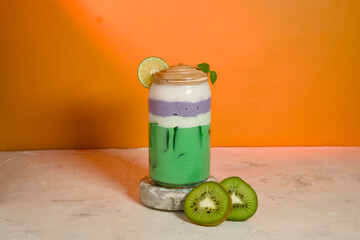 Iced colorful beverage with green and purple layers topped with foam and lime, perfect for tropical summer concept.