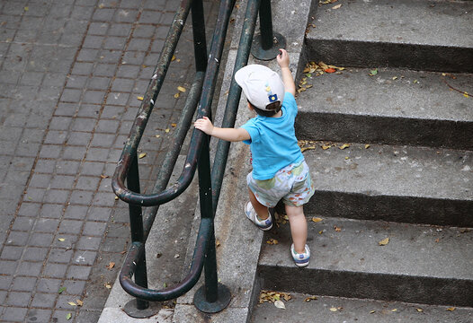 Ni&ntilde;o aprendiendo a andar dando sus primeros pasos subiendo escaleras con equilibrio y agarrado a la barandilla de la calle
