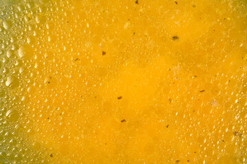 A very close-up shot captures the texture of clear yellow broth, showing small fat droplets and floating specks of herbs © nahhan
