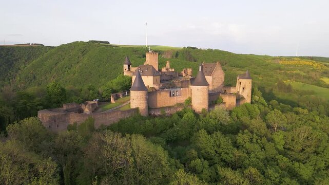 bourscheid castle ch&acirc;teau de green cover hills farms windmill hill behind cloudy sky complete bird&rsquo;s eye to left around right circling drone shot view 