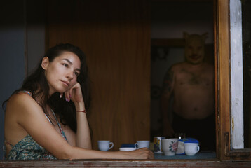 Woman at home by window with man in pig mask creating horror mood