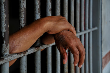 prisoner's hands behind bars with black background