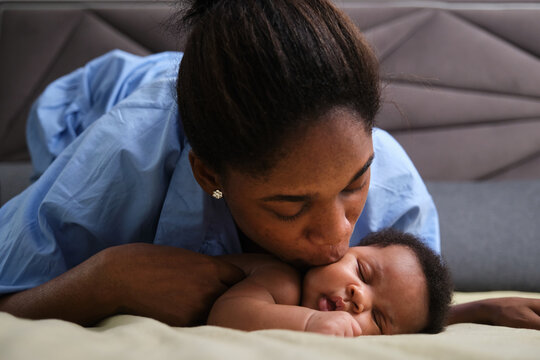 Tender moment of young woman kissing new born baby on bed