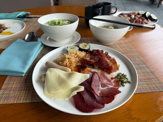 Diverse Vietnamese breakfast plate: bacon, cured meat, cheese, dried squid, traditional soup. Restaurant dining in Cam Ranh, Vietnam.
