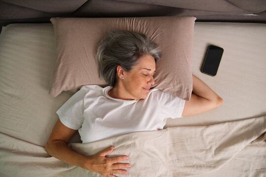 Person sleeping in bed with smartphone in a comfortable bedroom setting