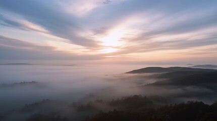 Naklejka premium Misty dawn over rolling hills, with soft golden sunlight piercing through layered clouds and fog blanketing the valleys below.