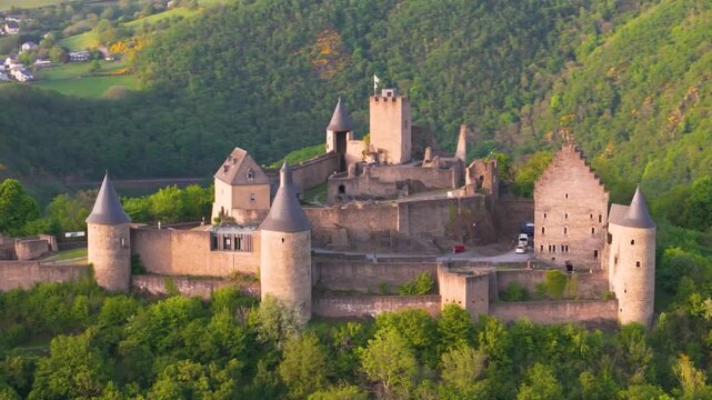 bourscheid castle ch&acirc;teau de green cover hills walls towers flags parked visitor vehicles beautiful town background to left near right drone panning shot 