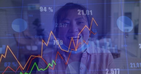 Smiling Asian male in pink shirt standing behind transparent financial charts in office, with mask