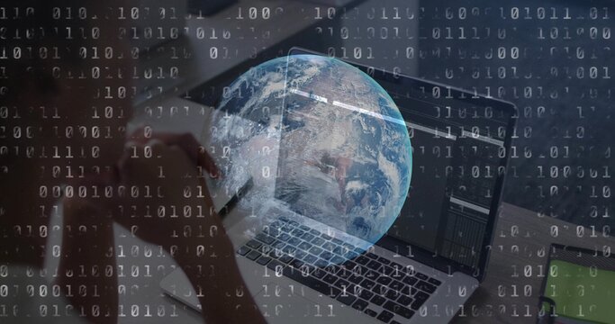 Typing mid-adult woman entering code on laptop at office desk, holding smartphone with binary globe