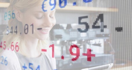 Smiling woman in business attire looking at tablet with floating ticker symbols at coworking office