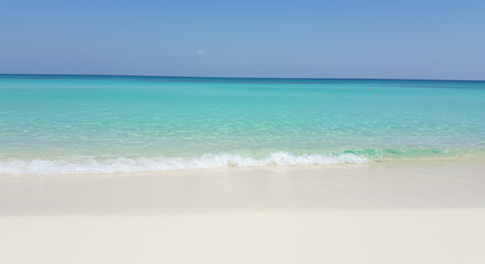 Crystal clear turquoise sea with gentle waves meeting a pristine sandy shore under a cloudless blue sky on a tranquil summer day