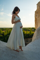 Pregnant woman in white dress standing outdoor in sunset time, Woman waiting for baby