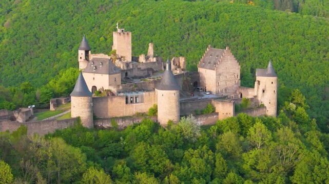 bourscheid castle ch&acirc;teau de green cover hills walls black domed towers visitor vehicles old historical site to left around right up close circling drone 