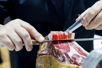 Professional chef slicing Iberico ham at gourmet kitchen in luxury restaurant. hands cutting cured...