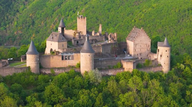 bourscheid castle ch&acirc;teau de green cover hills walls black domed towers visitor vehicles exterior views old historical to left near right up close circling drone shot 