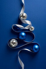 Vertical Christmas tree features blue ornaments, silver ribbon, and mirrorball accents against a...