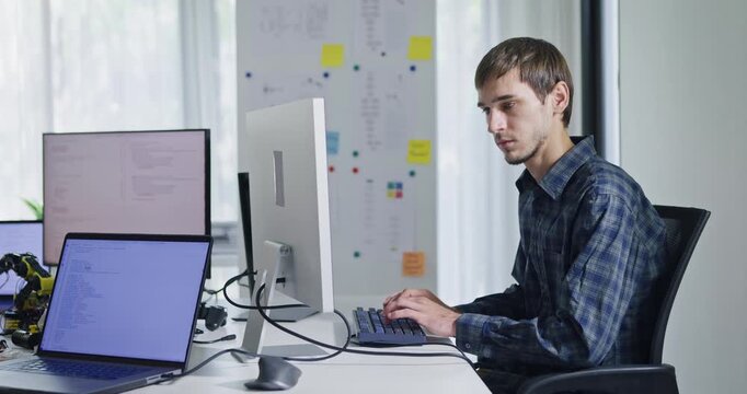 Portrait confident smiling male programmer working with robotics code AI software and looking at camera in tech office. Artificial intelligence dashboard, robotics, user interface, machine learning.