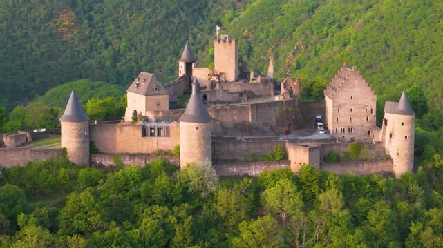 bourscheid castle ch&acirc;teau de green cover hills walls black domed towers visitor vehicles old historical site trees exterior to left around right circling drone shot 
