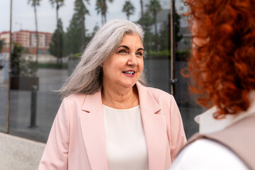 Confident mature businesswoman with gray hair smiling during outdoor conversation with colleague
