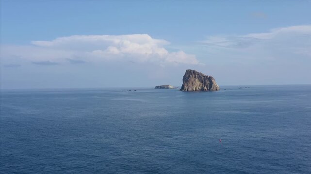 Aerial view of the stark, rocky Basiluzzo Islet rising from the deep blue sea under a clear sky, a serene contrast of textures and tones, Panarea, Sicily, Italy.