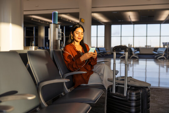Businesswoman using smartphone at airport terminal during sunset